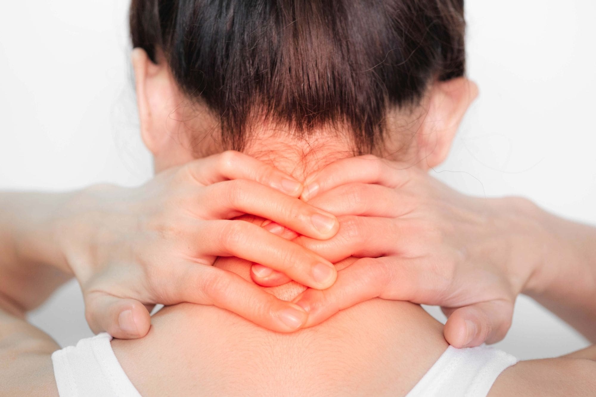 A person with dark hair holds the back of their neck with both hands, fingers interlaced, suggesting neck pain or tension. The area where their hands are placed appears slightly red.