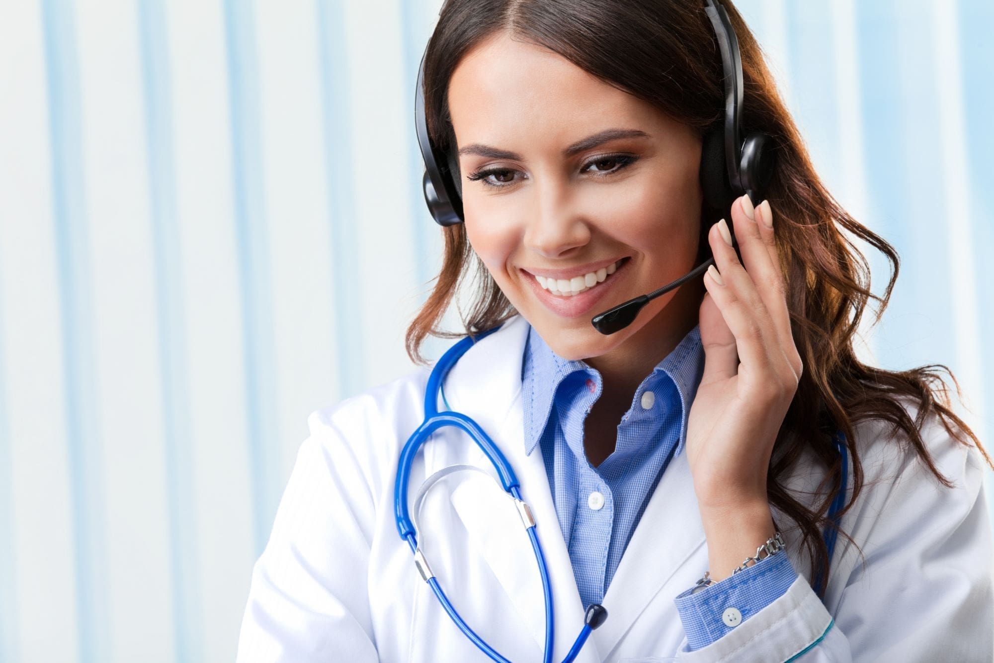 Smiling female doctor wearing a white coat and stethoscope, using a headset for a call or virtual consultation, with a blue and white striped background.