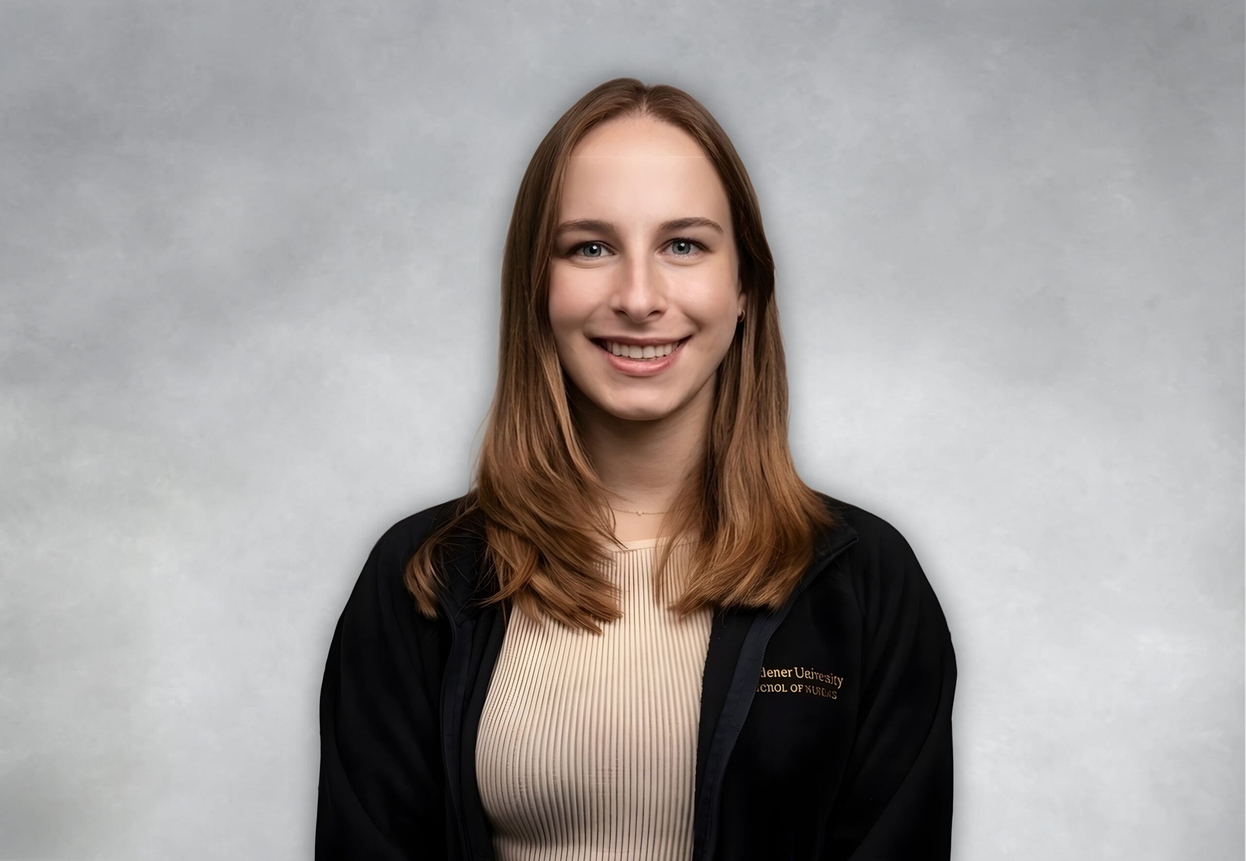 A young woman with straight, light brown hair smiles at the camera. She wears a beige top and a black jacket against a light grey background.