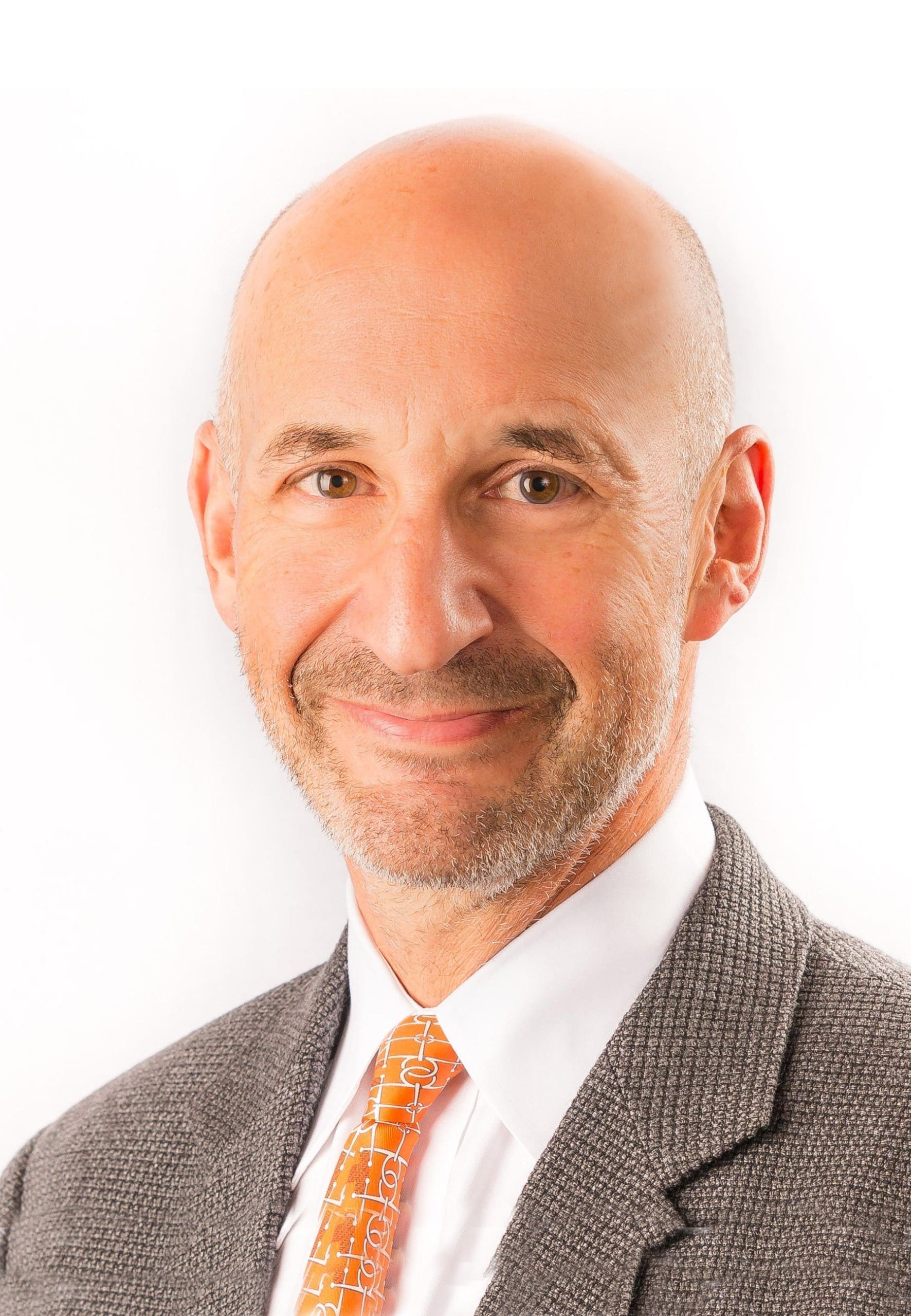 A middle-aged man with a bald head and short beard is smiling slightly. He is wearing a gray suit jacket, a white dress shirt, and an orange patterned tie, photographed against a plain white background.