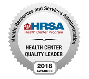 A round silver badge that reads Health Resources and Services Administration, HRSA Health Center Program, Health Center Quality Leader, 2018 Awardee.