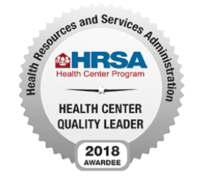 Silver badge displaying Health Resources and Services Administration, HRSA Health Center Program, Health Center Quality Leader, 2018 Awardee with a house and people logo at the top.
