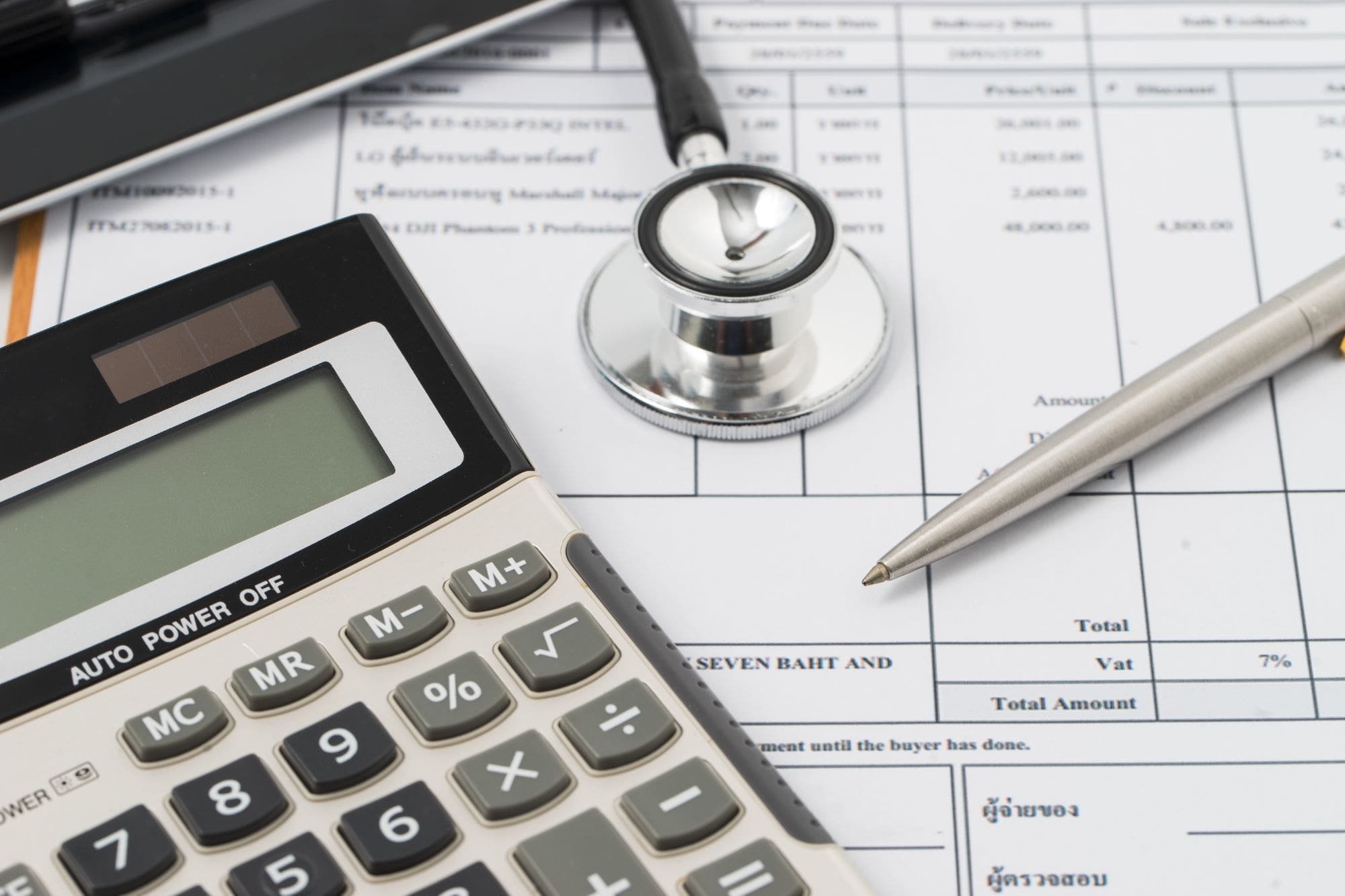 A calculator, stethoscope, and pen resting on a medical bill or financial document, symbolizing healthcare expenses and medical billing.