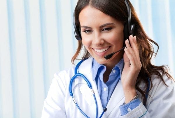 Smiling female doctor wearing a white coat and stethoscope, using a headset for a call or virtual consultation, with a blue and white striped background.