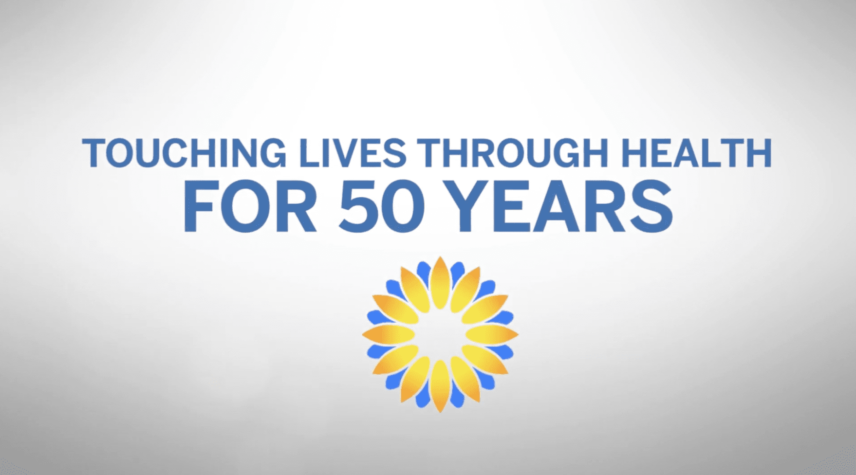Blue text reads “Touching Lives Through Health For 50 Years” above a yellow and blue flower-like logo, on a white background.