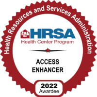 A circular red and white badge with the text Health Resources and Services Administration, HRSA Health Center Program, Access Enhancer, 2022 Awardee and a small house with medical symbols.