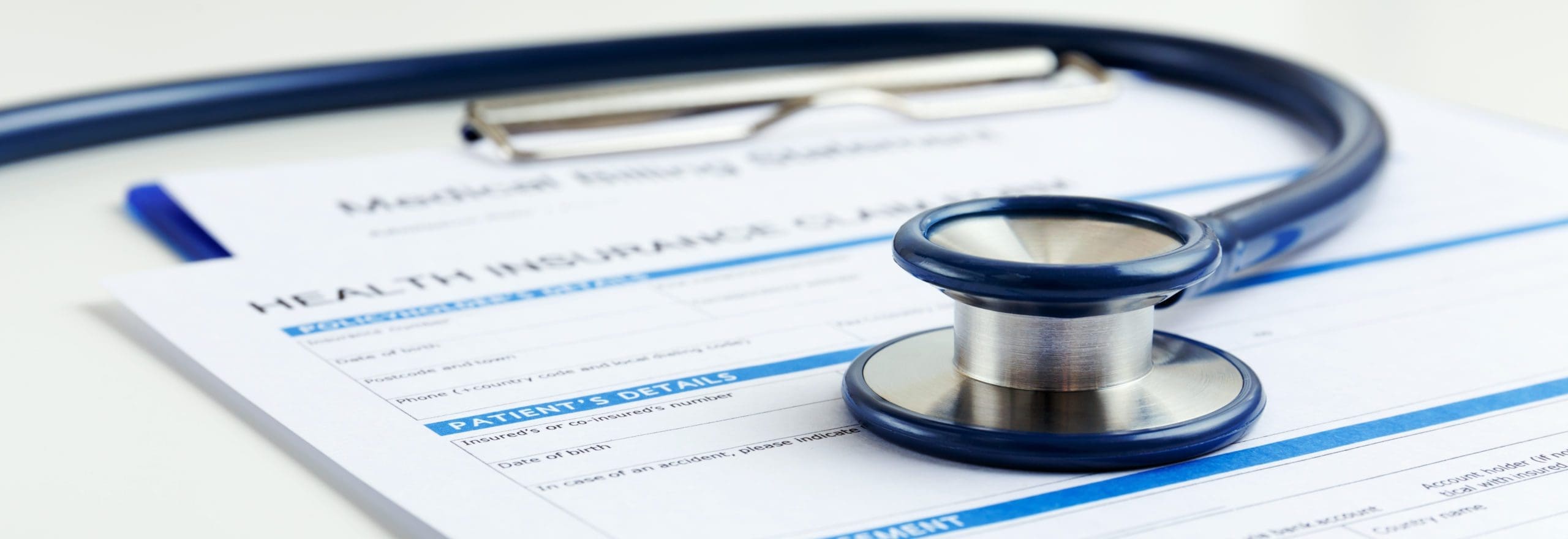 A stethoscope and clipboard rest on top of a health insurance claim form, highlighting the connection between healthcare and insurance paperwork.